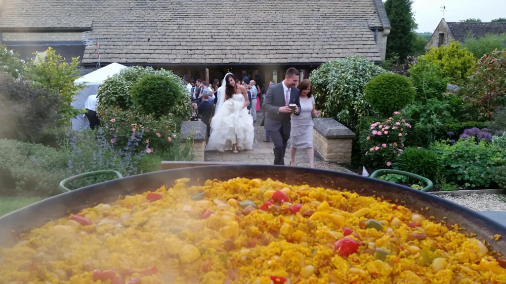 Bride and wedding guests walking towards freshly cooked Spanish paella at a beautiful countryside wedding venue in the UK.